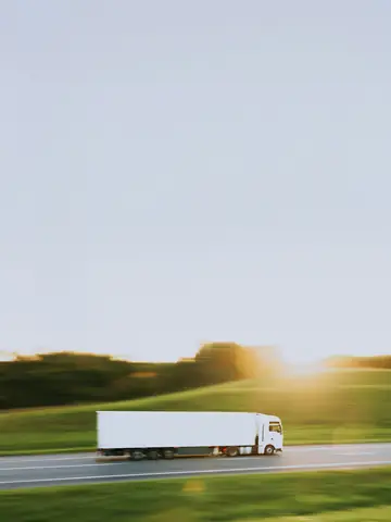 Vit lastbil med trailer på en motorväg i kvällssol
